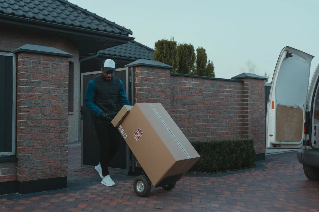 Umzugshelfer bringt einen Karton mit der Sackkarre zum Transporter