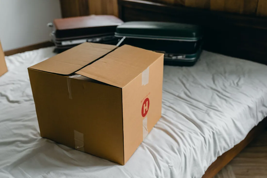 Gepackter Umzugskarton und Koffer auf dem Bett eines WG-Zimmers